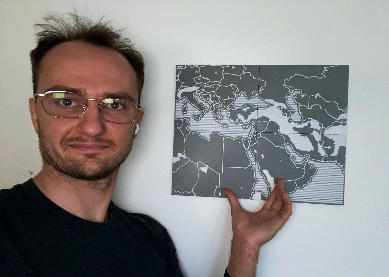 Gleb stoji pored sklopljene taktilne karte okačene na zid, sa rukom naslonjenom na nju.